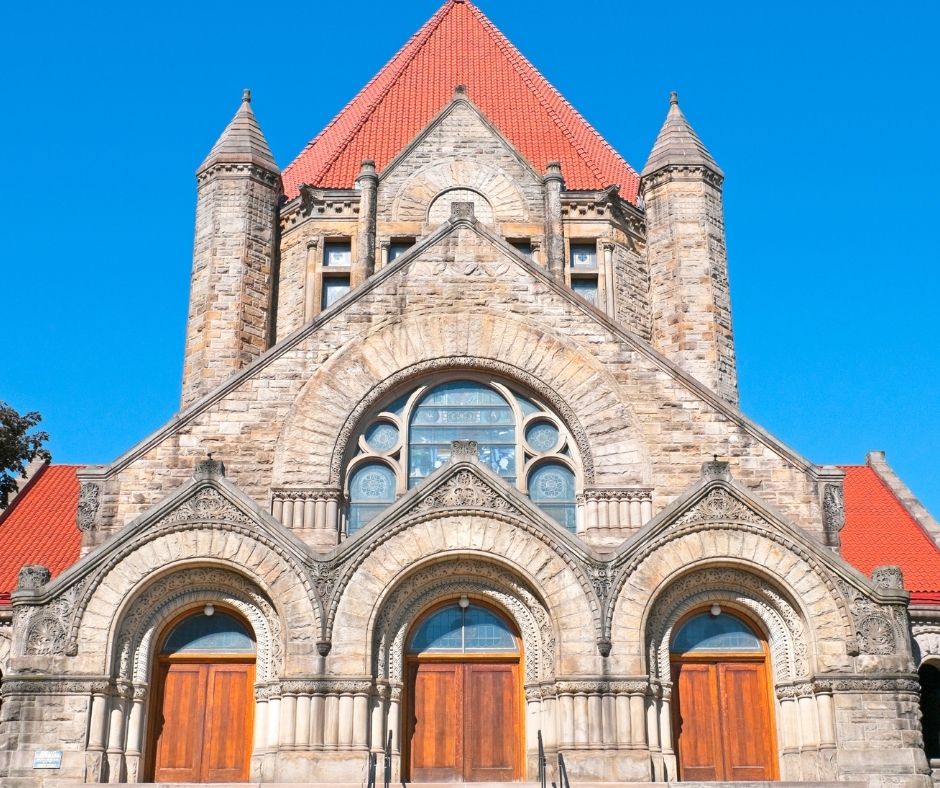 Stone façade of Pittsburgh’s First United Methodist Church with arched wooden doors, decorative windows, and a red-tiled roof.